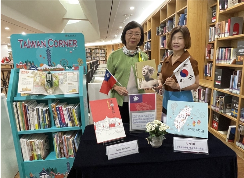 Director General Tseng and Seoul Metropolitan Library's Seon Myeonghwa holding their respective flags in front of the Taiwan Corner